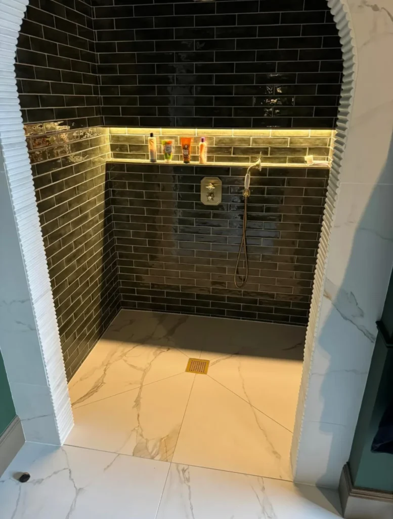 Walk-in shower with dark brick style tiles, recessed shelf and porcelain shower floor installed by Stamford tiler.