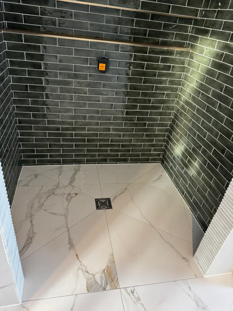 Walk-in shower tiling with dark wall tiles and large format marble effect floor tiles installed by Stamford tiler covering Stamford, Oakham and Uppingham.