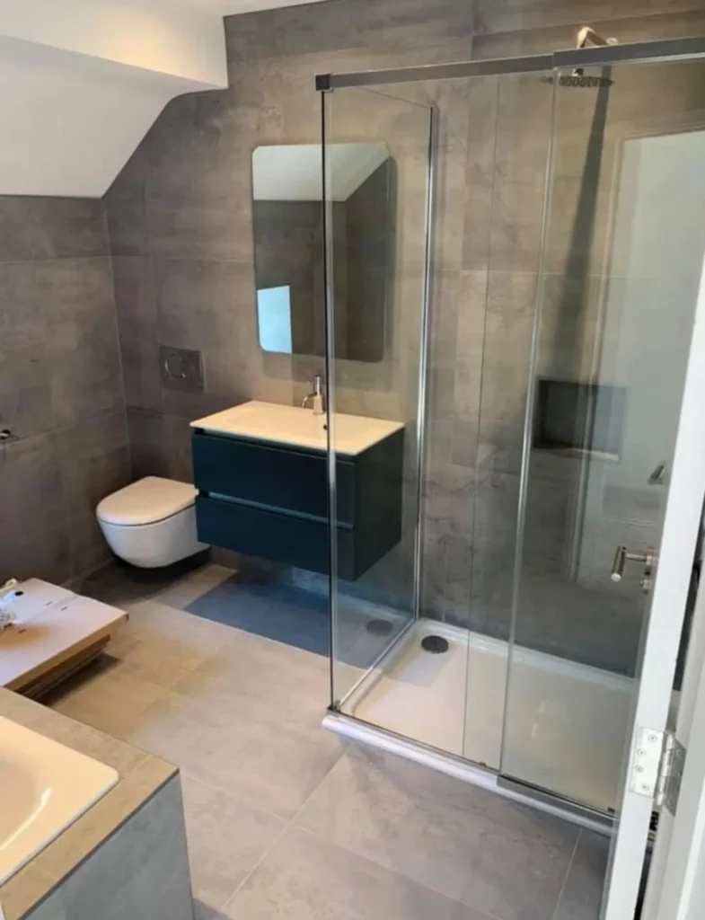 Modern bathroom with large format grey tiles and glass shower enclosure installed by Stamford tiler.