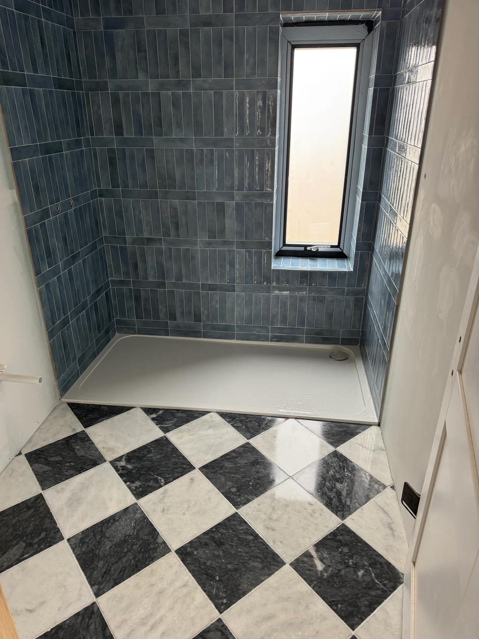 Bathroom tiling with dark wall tiles and black and white patterned stone floor installed by Stamford tiler serving Stamford, Oakham and Uppingham.
